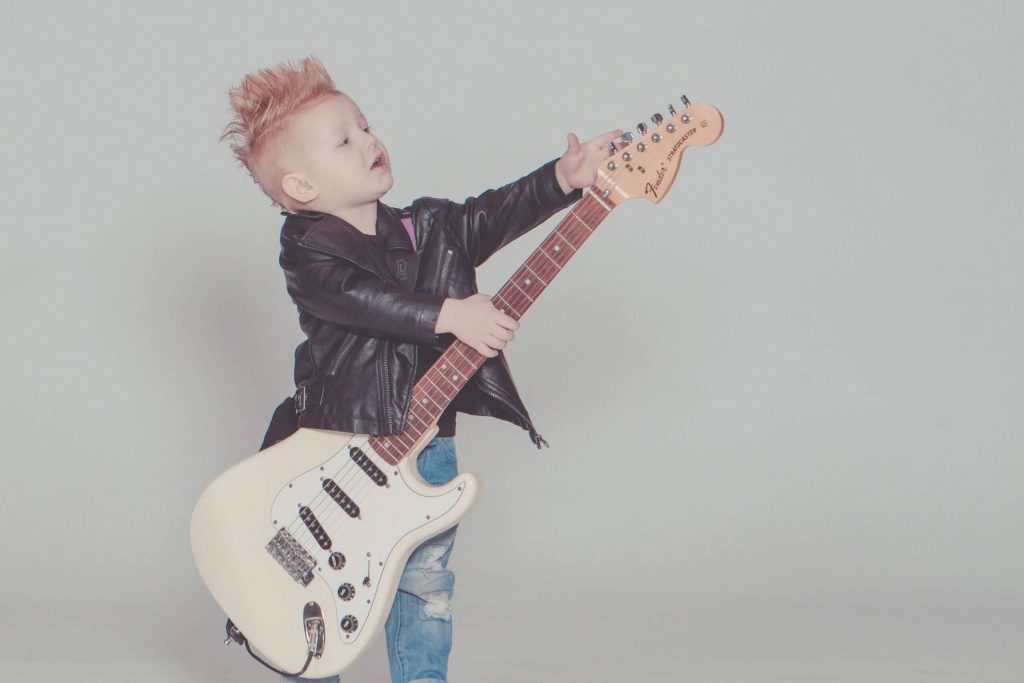 Effects of Music on Child Development - A little boy with spikey hair in a leather jacket attempts to tune an electronic guitar.