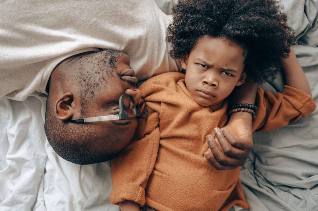 Helping Preschoolers Cope With Their Emotions - A child lying with their father displays an angry face.