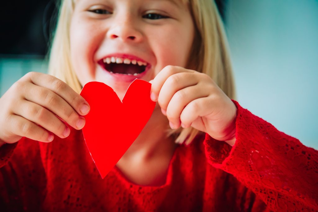 happy little girl holding paper heart in hands. Valentine's day crafts. 