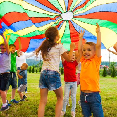 Happy laughing boy standing hands-up under colorful cloth. Children having fun on the birthday party